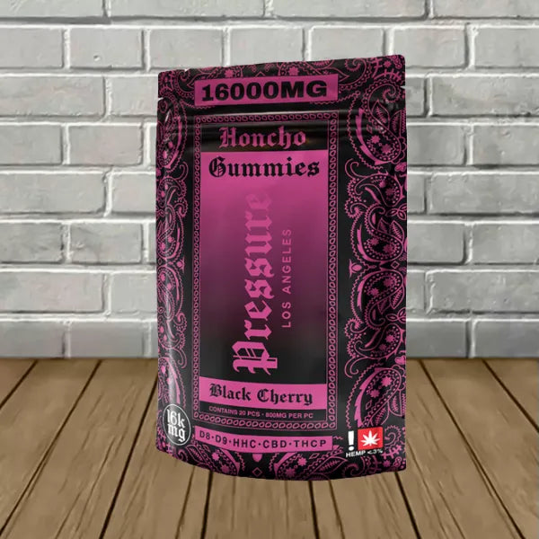 Purple and black package of Pressure LA 16000mg Honcho Gummies, Black Cherry flavor, on wooden surface against brick wall. Product features ornate design and cannabinoid content information.